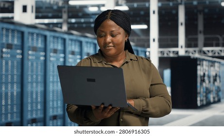 Coder in server facility working with notebook computer to update systems for increased stability. IT professional in server environment setting up infrastructure with notebook for optimum performanc.