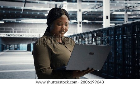 Coder in server facility working with notebook computer to update systems for increased stability. IT professional in server environment setting up infrastructure with notebook for optimum performanc.