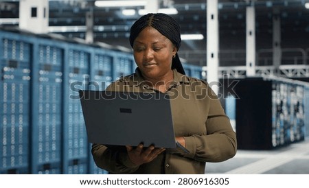 Coder in server facility working with notebook computer to update systems for increased stability. IT professional in server environment setting up infrastructure with notebook for optimum performanc.