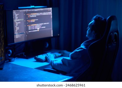A coder is working late at night on a computer, using a code editor and a smartphone app, as seen from the back view