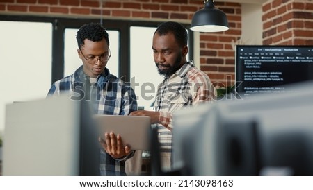 Coders talking about algorithms holding laptop pointing at sorce code on screen standing in software developing office. Team of coders discussing cloud computing in programming enviroment.
