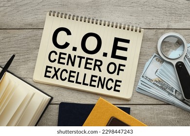 C.O.E Center Of Excellence. text on a page of a notebook near a yellow notebook with a magnifying glass and banknotes of money