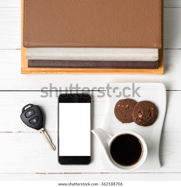 coffe cup with cookie,phone,car key and stack of\
book on white wood table