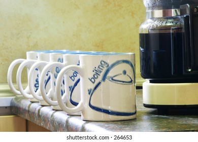 Coffe mugs lined up next to coffee pot
