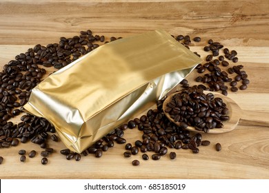 Coffee Bag And Packaging. The Gold Foil Bag On The Wood Table With Dark Roasted Coffee Beans.