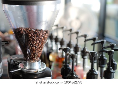 Coffee beans in bean hopper, part of coffee machine, with syrup bottles.