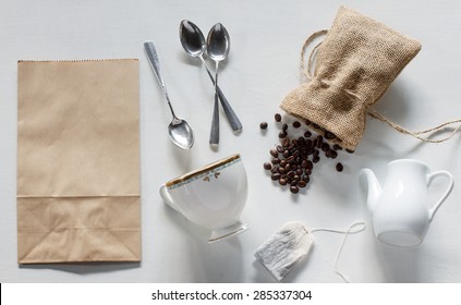 coffee beans in burlap bag, paper bag, silver spoon, vintage cup, white jar, teabag on white wood background. - Powered by Shutterstock