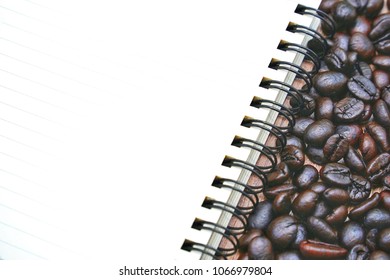 Coffee beans and empty note book isolated on wooden table desk with workspace. Copy space empty blank for text.