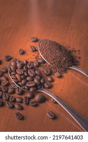 Coffee beans and ground coffee beans in 2 different spoons, close-up top view and on brown wooden floor.