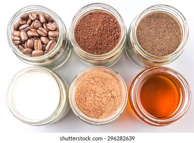 Coffee Beans, Coffee Powder, Creamer, Cocoa Powder, Honey And Processed Tea Leaves In A Mason Jar Over White Background