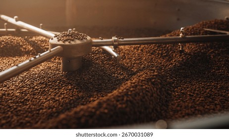 Coffee beans rotating inside cooling tray under moving metal arms of industrial roasting machine. Spreading evenly for consistent temperature. Preparing beans for grinding or packaging.