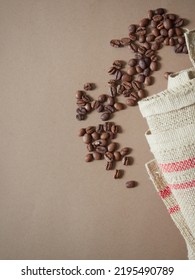 Coffee Beans Scattered On A Plain Brown Background Next To A Burlap Sack. Flat Lay With Copy Space