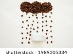 Coffee beans in shape of cloud pouring raindrops above an inverted cup as an umbrella. White background, isolated
