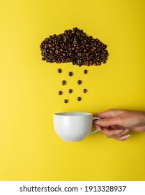 Coffee beans in shape of rainy cloud with white cup on yellow background. Creative minimal coffee drink concept.