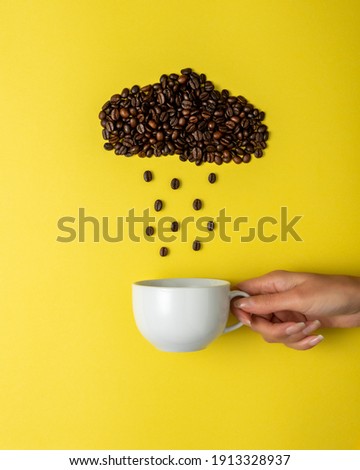 Coffee beans in shape of rainy cloud with white cup on yellow background. Creative minimal coffee drink concept.