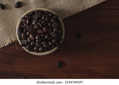 Coffee Beans In A Small Brown Bowl Sat On Top Of A Wooden Table. Flat Lay Coffee Theme Image. Brown Monochromatic Rustic Food Photo With Copy Space