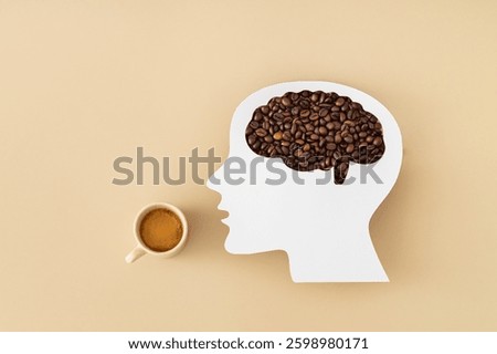 Coffee beans visible through a head profile with brain shaped paper cutout and cup of coffee on beige background. Creative coffee concept. Trendy coffee addiction idea. Flat lay style.