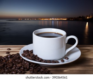 Coffee beans and coffee in white cup on wooden table opposite a defocused natural landscape for background. Collage. Selective focus. - Powered by Shutterstock