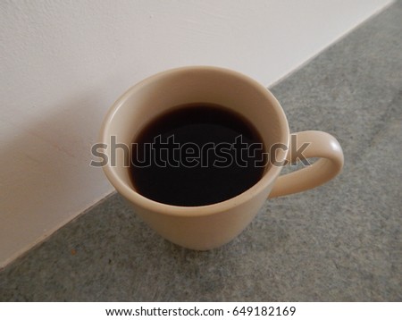 Coffee in beige mug on marble worktop against magnolia wall. Worktop line cuts diagonally from top right to bottom left. Macro