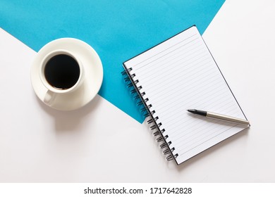 Coffee and blank notebook on split color blue and white background. Flat lay with copy space. Business concept