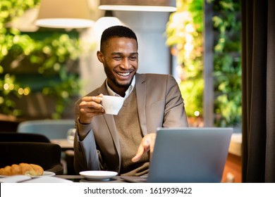 Coffee Break In Cafe. Millennial Black Man Working In Cafeteria, Using Laptop, Holding Cup, Empty Space