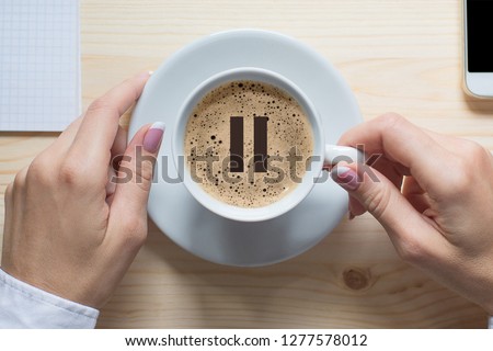 Coffee break. Female hands touches white cup of classic coffee, top view, close up. Pause icon on foam. Pause, break, short breather, relax, pit stop in the middle of business life.