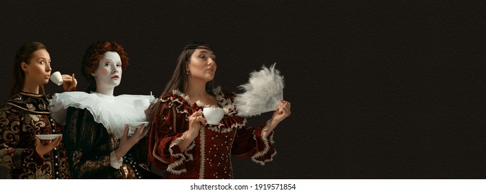 Coffee break for queens. Medieval people as a royalty persons in vintage clothing on dark background. Concept of comparison of eras, modernity and renaissance, baroque style. Creative collage. Flyer - Shutterstock ID 1919571854