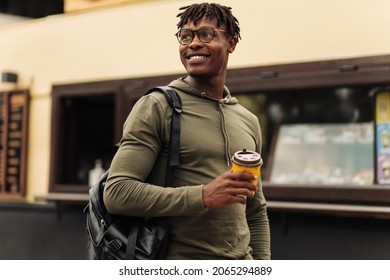 Coffee Break For Student, Handsome African American Male Student, Wearing Glasses And With A Backpack On His Shoulder, Drinking Coffee On The Street In The City