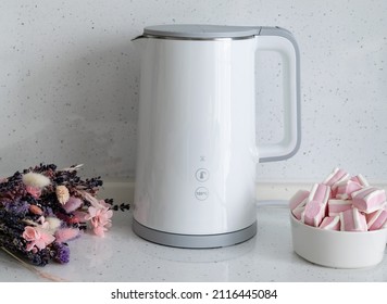 Coffee Break With Sweets. On The Countertop Of A Bright Marshmallow Kitchen Next To A White Electric Kettle And A Bouquet Of Flowers.