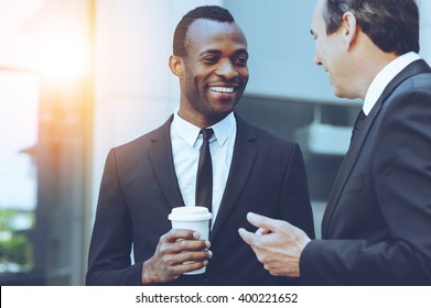 Coffee break. Two cheerful business men talking while one of them holding coffee cup