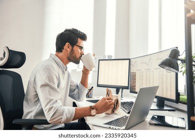 Coffee break. Young bearded businessman or trader is drinking a coffee and eating a sandwich while looking at monitor screen with financial data in his modern office - Powered by Shutterstock