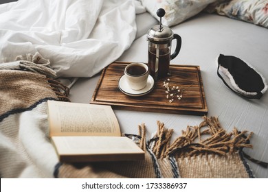 Coffee brewed in a French press and a cup on a wooden board with open book in bed. Morning at home, coziness and comfort. - Powered by Shutterstock