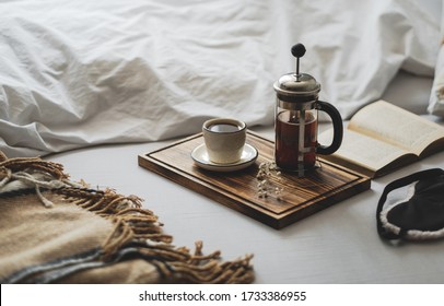 Coffee brewed in a French press and a cup on a wooden board with open book in bed. Morning at home, coziness and comfort. - Powered by Shutterstock