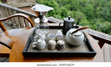 a coffee brewing setup on a wooden table overlooking a lush green landscape. A sleek pour-over coffee maker, complete with filter and glass carafe, takes center stage. - Powered by Shutterstock