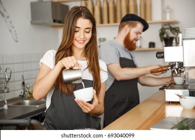 Coffee Business Concept - close-up lady barista in apron preparing and pouring milk into hot cup while standing at cafe. - Powered by Shutterstock