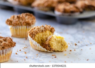 A Coffee Cake Muffin, With A Bite Taken Out On A Table With Muffin Tin In Background.  Horizontal