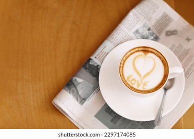 Coffee, cappuccino and heart in foam with newspaper on a table with no people in a restaurant. Cafe drink, love writing and foamy beverage art with milk in a cafe with a closeup of mug and mockup - Powered by Shutterstock