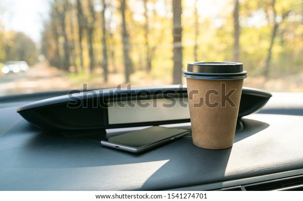 Coffee in car. Brown coffee cup and phone on car\
console (panel).