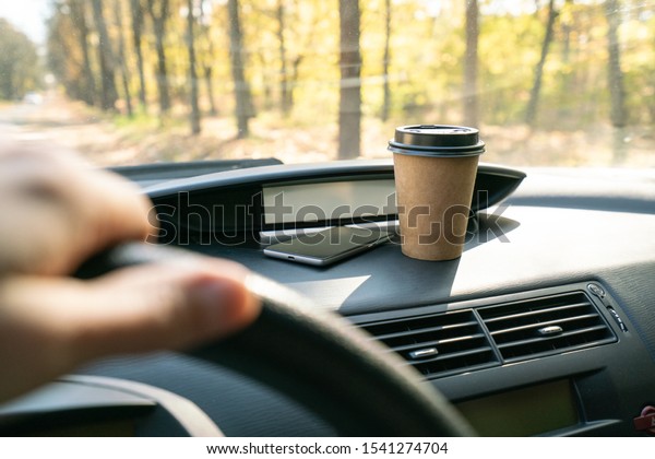 Coffee in car. Brown coffee cup and phone on car\
console (panel).