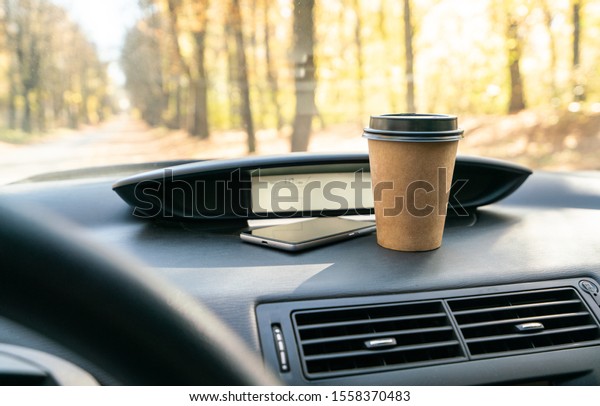 Coffee in car. Brown coffee cup and smartphone\
on car console (panel).