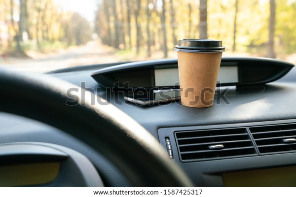 Coffee in car. Coffee cup and smartphone on car\
console (panel)