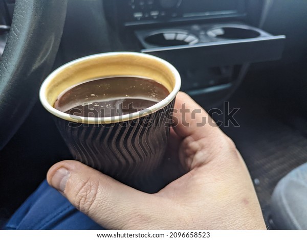 coffee in the car. Man\
holding coffee paper cup in car. coffee is a friend of traveler.\
transportation and vehicle concept - man drinking coffee while\
driving the car. 