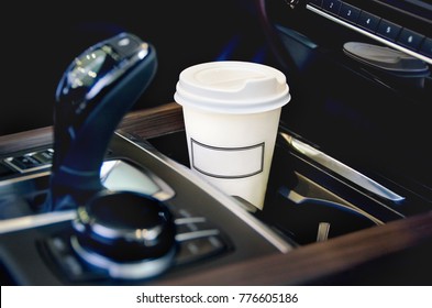 Coffee in the car salon. A single paper coffee cup inside the car cup holder.