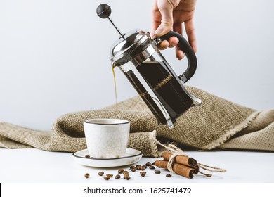 coffee composition. A female hand pours brewed coffee in a French press into a white handmade cup with a black rim. White background, coffee beans, cinnamon sticks - Powered by Shutterstock