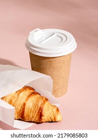 Coffee in a craft paper cup and croissant on pink background with  foliage shadow. Sunny urban scene with hard light and shadow. Breakfast to go, take away food concept.