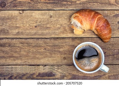 Coffee and croissant for breakfast on rustic wooden table, top view 