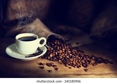 Coffee cup and coffee beans on a wooden table and sack background,Vintage color tone