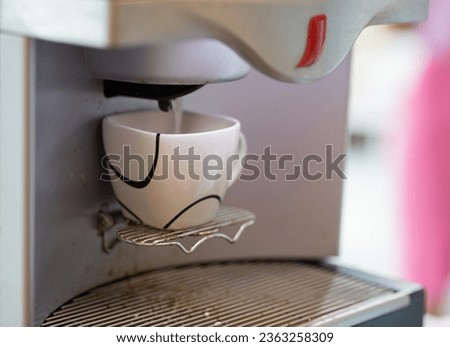 The coffee cup is being placed on the automatic coffee maker.