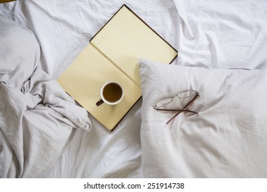 Coffee cup, book, reading glasses on bed - Shutterstock ID 251914738