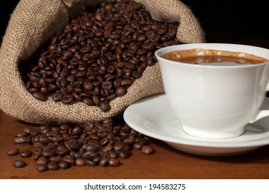 Coffee cup with burlap sack of roasted beans against dark wood background